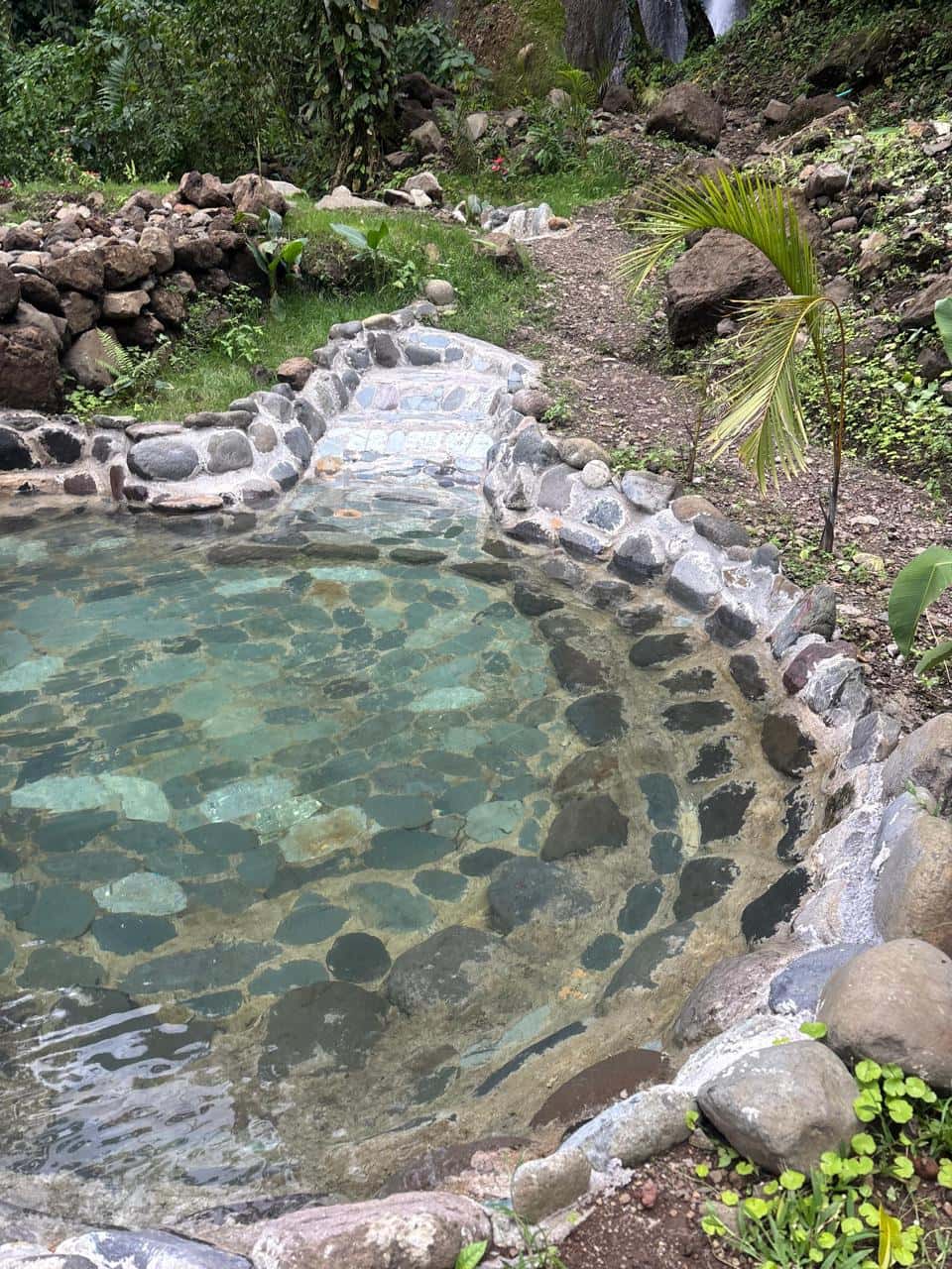 Poza termal de piedra con escalones, bajo la catarata