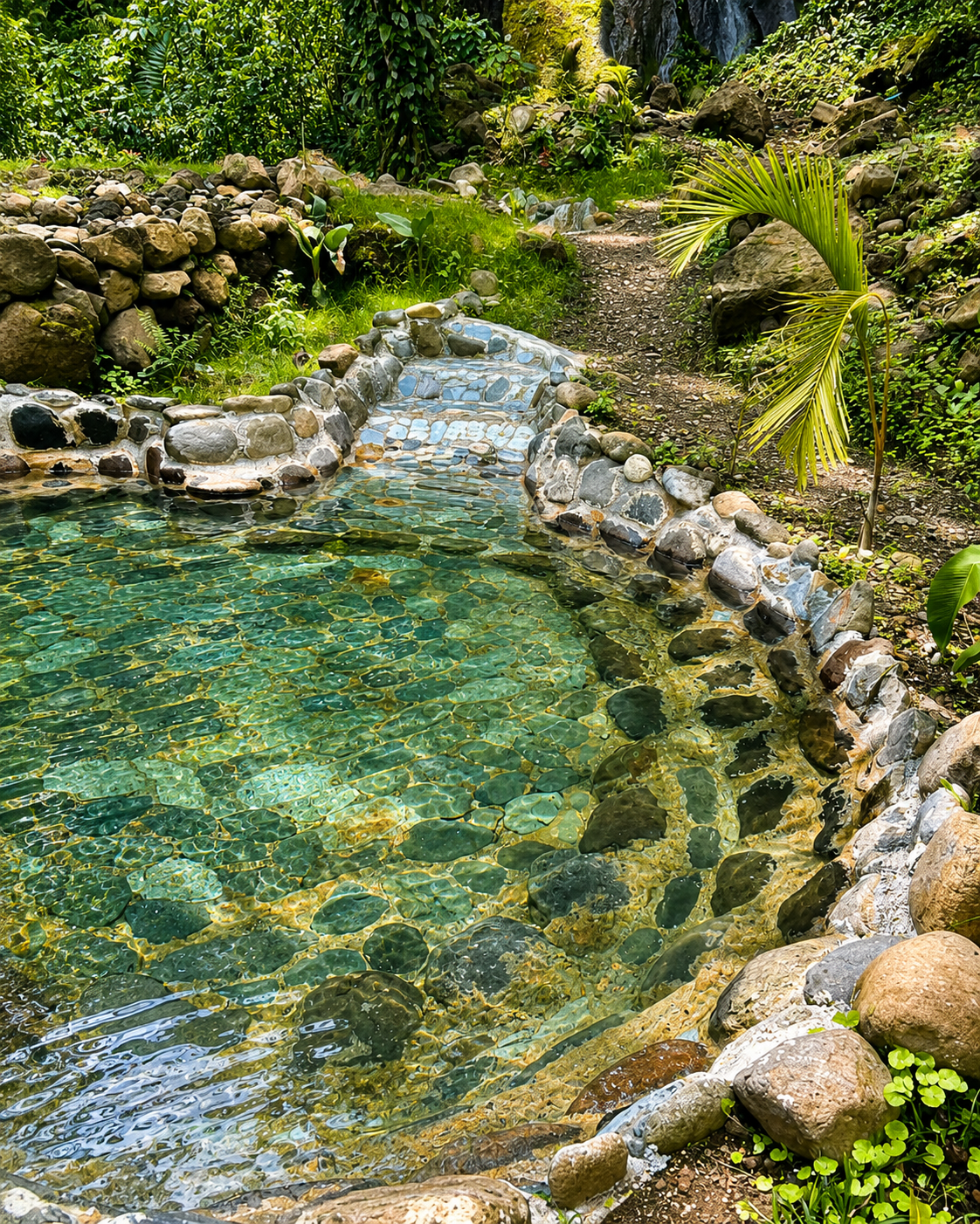Poza termal de agua color jade entre piedras de río y selva